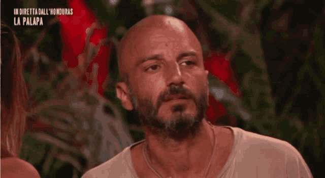 a bald man with a beard is wearing a white shirt with a necklace around his neck