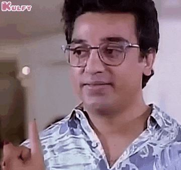 a man wearing glasses and a blue shirt is pointing at something with his finger .
