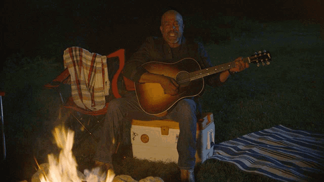 a man is playing a guitar in front of a campfire