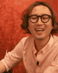 a man wearing glasses and a pink shirt is laughing .