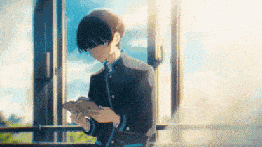 a young boy is reading a book while standing in front of a window .