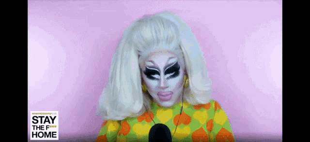 a drag queen is talking into a microphone while wearing a wig and makeup .