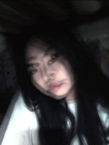 a woman with long black hair is taking a selfie in the dark while wearing a white shirt .