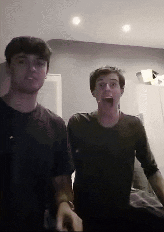 two young men are standing next to each other and one of them is making a surprised face .