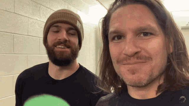 two men standing next to each other with one wearing a green shirt