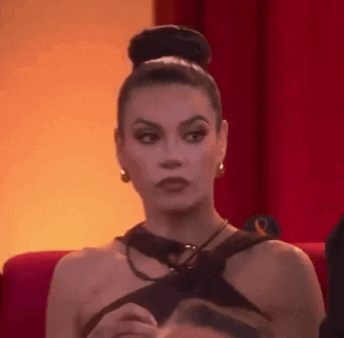 a woman in a bun is sitting in front of a red curtain and looking at the camera .
