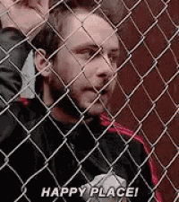 a man is behind a chain link fence and saying `` happy place ! ''