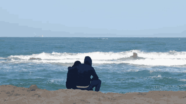 a man and a woman sit on a beach looking at the ocean
