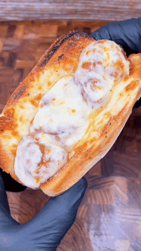 a person wearing black gloves is holding a meatball sub with cheese