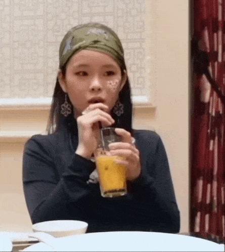a woman is drinking a glass of orange juice while wearing a bandana .