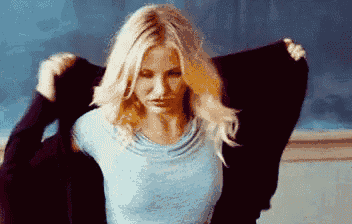 a woman is taking off her sweater in front of a chalkboard .