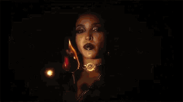 a woman is holding a red rose and a candle in her hand in the dark .