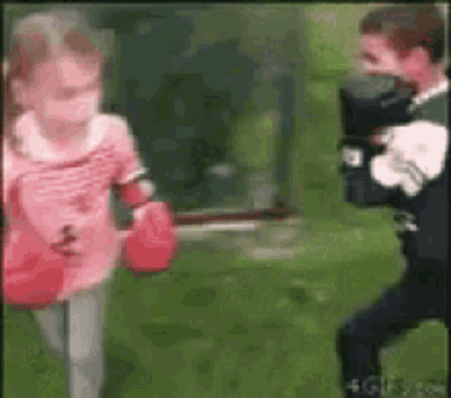 a boy and a girl are boxing in the grass . the girl is wearing red boxing gloves .