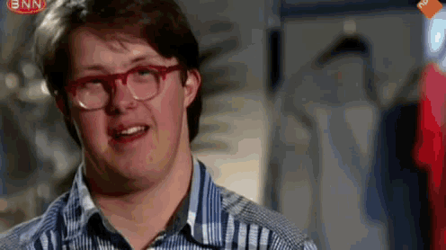 a man wearing glasses and a plaid shirt is smiling in front of a bnn sign