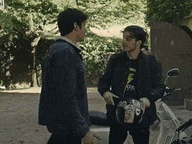 two men are standing next to each other and one is holding a helmet with a sticker on it .