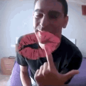 a man in a black shirt is holding a red lip in his mouth and giving the middle finger