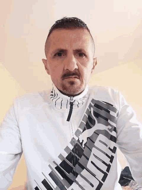 a man with a beard is wearing a white puma shirt and looking at the camera .