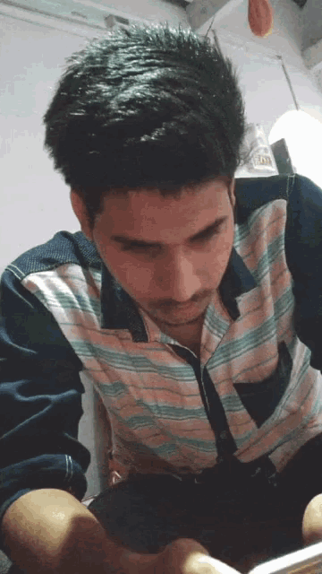 a man wearing a striped shirt is looking down at something