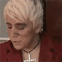 a woman wearing a red jacket and a cross necklace is looking down .