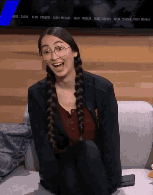 a woman wearing glasses is sitting on a couch in front of a screen that says ' fox news ' on it