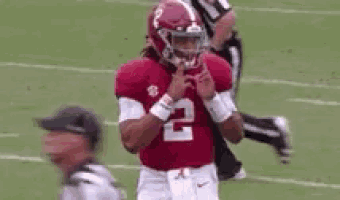 a football player wearing a red jersey with the number 2 on it is making a peace sign on the field .
