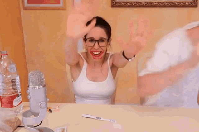 a woman in a white tank top is sitting at a table with a microphone and a bottle of water