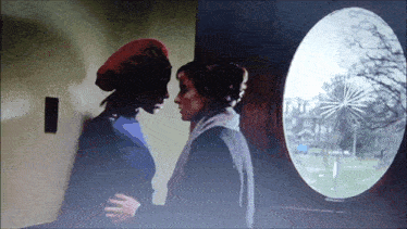 a woman in a red beret stands next to another woman in front of a round window