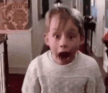 a young boy is making a surprised face while wearing a white sweater .
