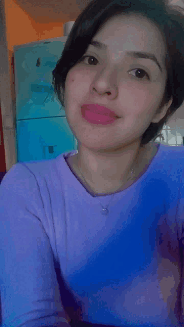 a woman in a purple shirt is taking a selfie in front of a refrigerator