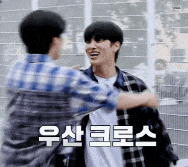 two young men hugging each other in front of a fence with korean writing on it