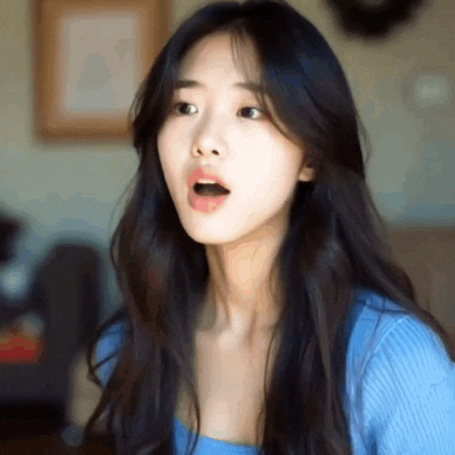 a woman with long black hair is wearing a blue sweater and has her mouth open .
