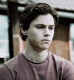 a young man wearing a purple t-shirt is looking at the camera .