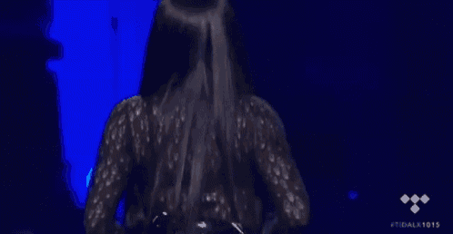a woman in a black dress is standing on a stage with her hair being poured on her .