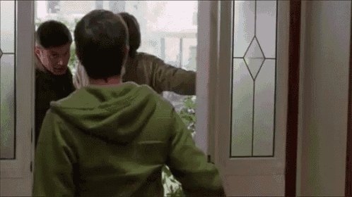 a man in a green hoodie is standing in front of a door with two other men .