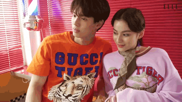 a man wearing an orange gucci t-shirt stands next to a woman wearing a purple sweater