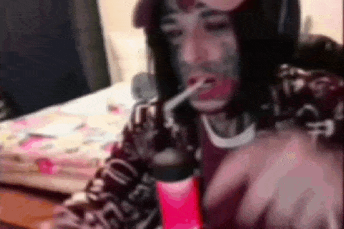 a man with a tattoo on his face is smoking a cigarette in a room .