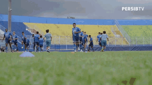 a group of soccer players are running on a field in front of a stadium .