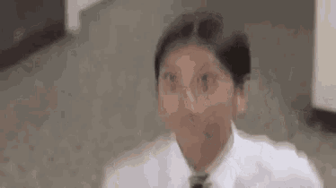 a young girl in a white shirt and tie is sitting on the floor and looking at the camera .