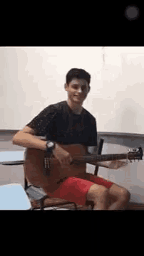 a young man is playing an acoustic guitar in a classroom .