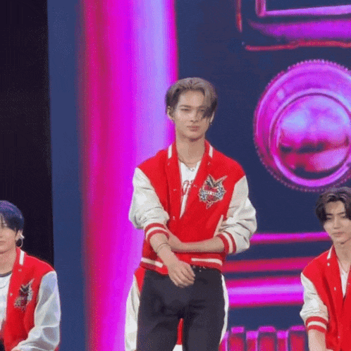 a man in a red and white varsity jacket is standing on a stage with his arms crossed .