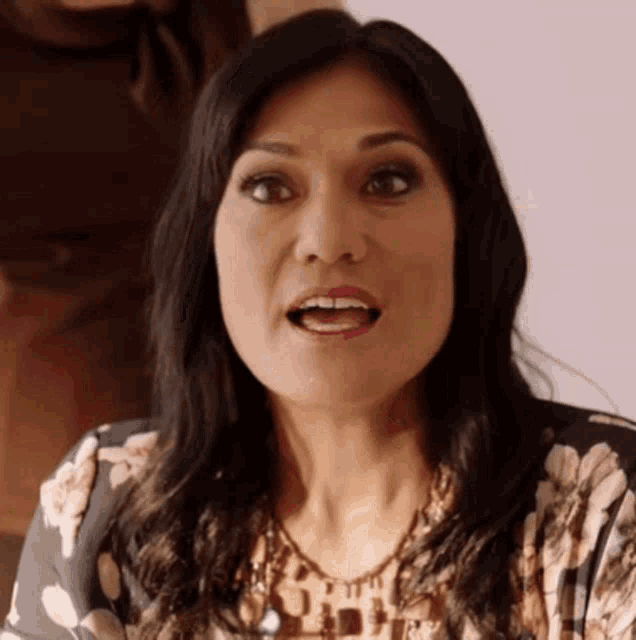 a woman in a floral shirt is making a surprised face .