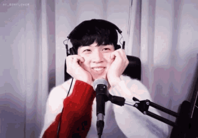 a young man wearing headphones and a red and white sweater is smiling in front of a microphone .