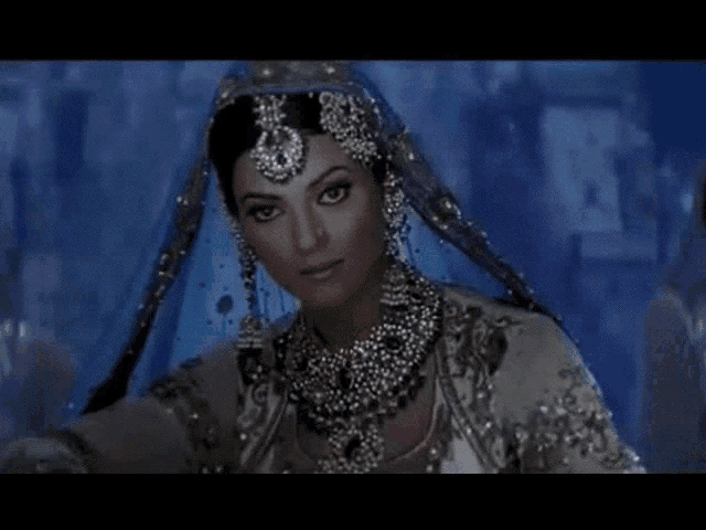 a woman wearing a veil and jewelry is looking at the camera .