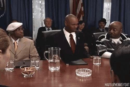 a man in a suit and tie sits at a table with a pitcher of water and a bowl of peanuts