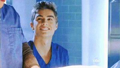 a young man in a blue scrub top is smiling in a room .