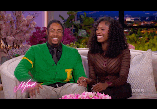 a man in a green cardigan with the letter i on it sits next to a woman