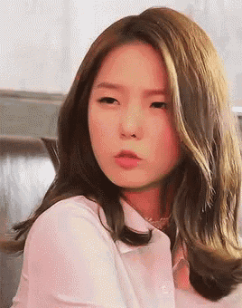 a close up of a woman 's face with a pink shirt on looking at the camera .