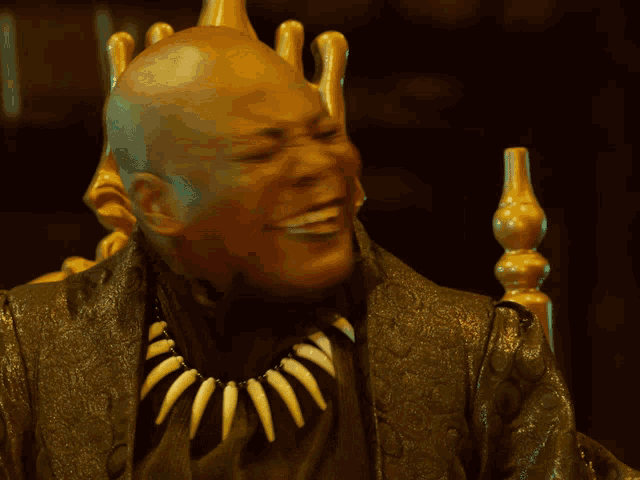 a man with a necklace of fangs is sitting in a gold chair