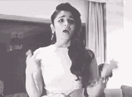 a black and white photo of a woman in a white dress standing in a living room .