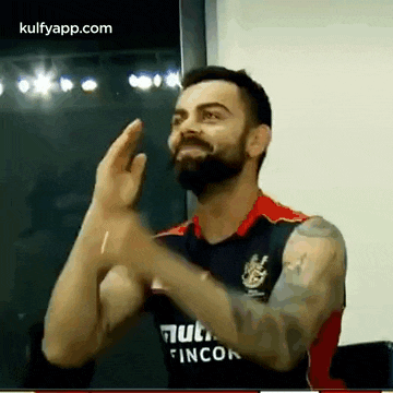 a man with a beard and tattoos is clapping his hands in a room .